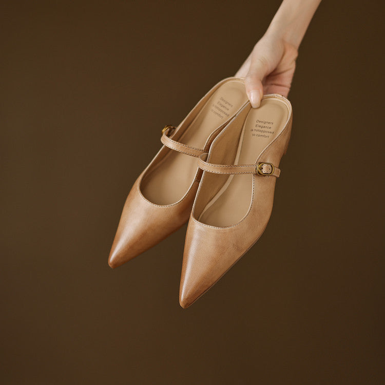 Tan leather mules held in hand, pointed toe and ankle strap with buckle