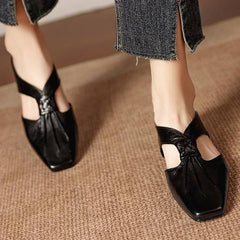 Black square-toe leather mules with knotted bow detail and low heel.