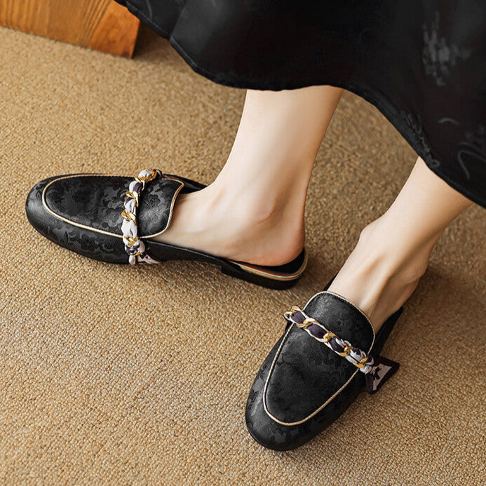 Black leather mules with rounded toe and gold-toned chain strap detail