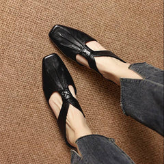 Black square-toe leather mules with knotted bow vamp, worn with jeans.