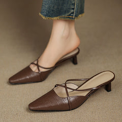 Brown genuine leather mules with crisscross straps and mid heel, worn with jeans cuffs.