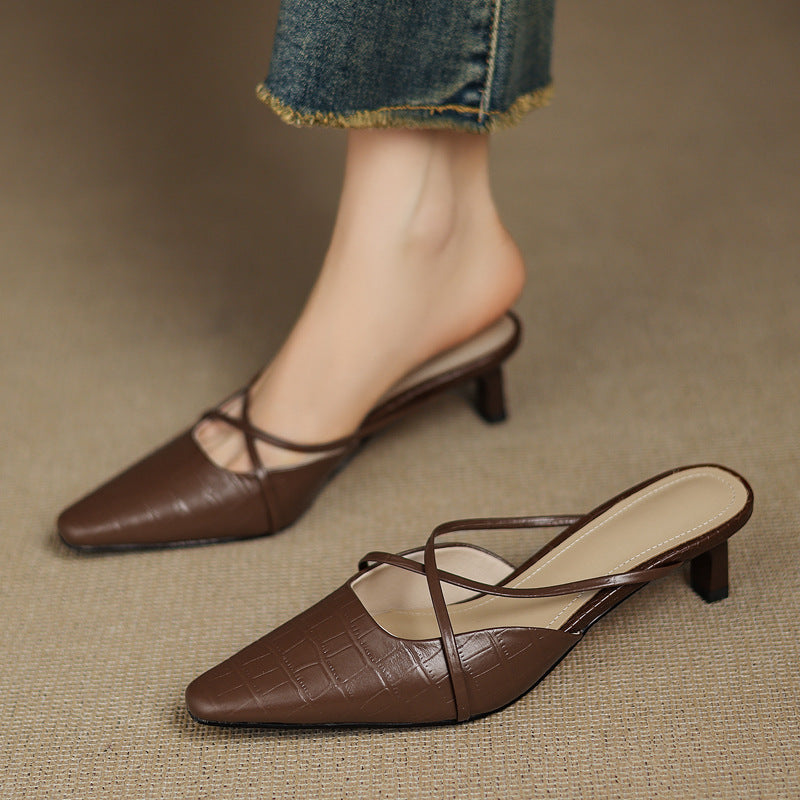 Brown genuine leather mules with crisscross straps and mid heel, worn with jeans cuffs.
