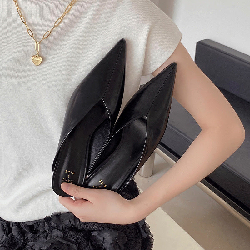 Black pointed-toe slip-on mules held in hand, low heel