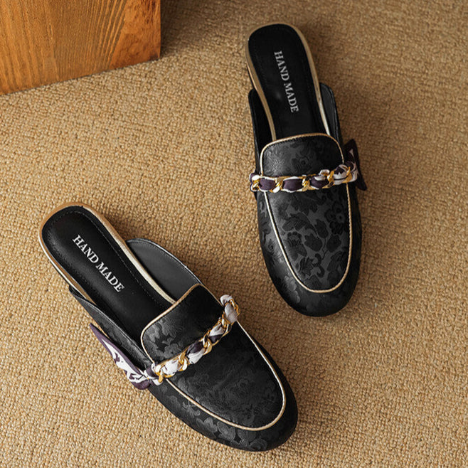 Black patterned leather mules with gold chain trim and bow on the vamp