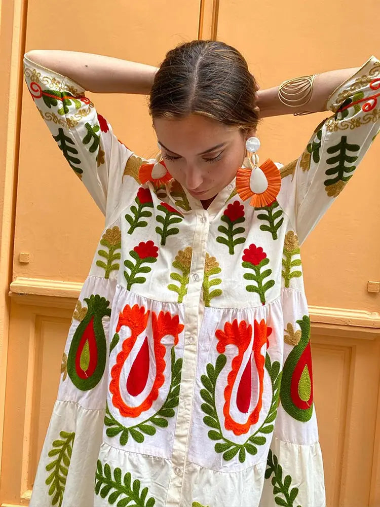 White peasant-style dress with V-neck, long sleeves, and colorful folk flower print