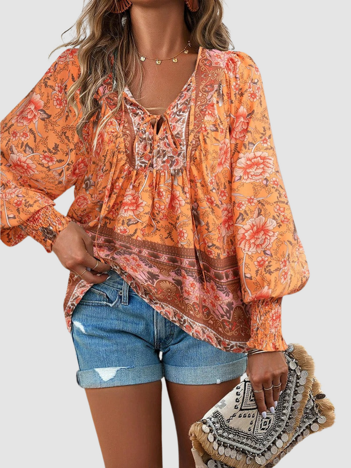 Orange floral peasant blouse with V-neck tie, smocked yoke, and billowy long sleeves.