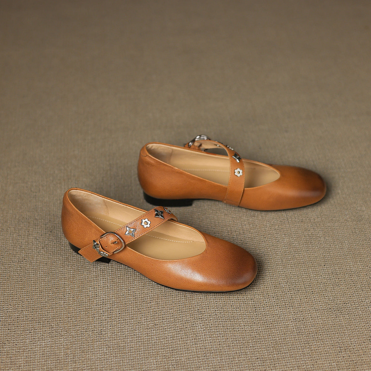 Pair of tan leather flats with buckle strap and star-flower ornament on vamp