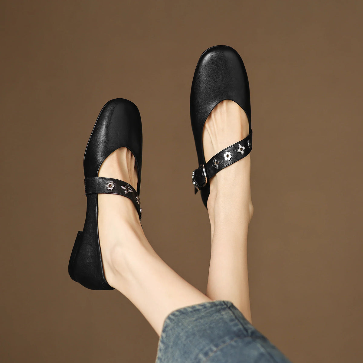 Black leather flats with strap and buckle; star-flower accents on outer strap