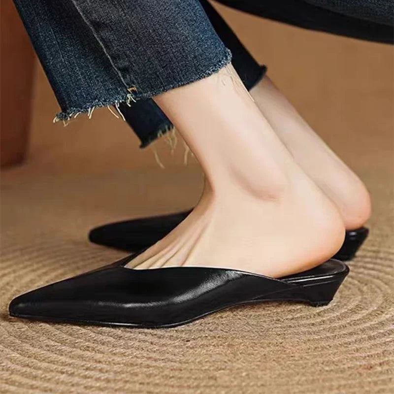 Black leather pointed-toe mule with low heel, close-up on foot.