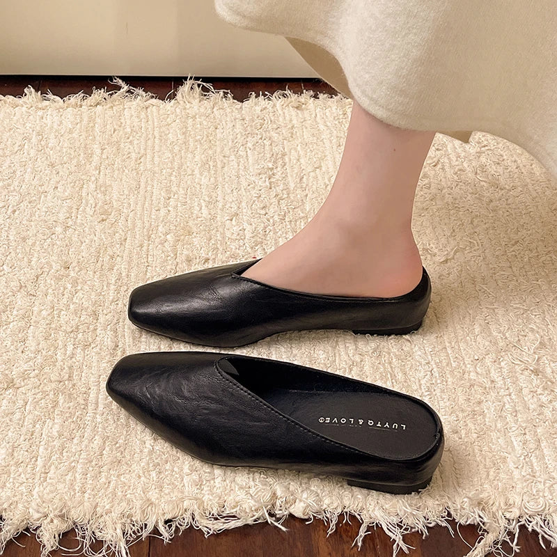 Black pointed-toe mules with low flat sole, slip-on backless style.