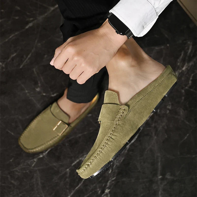 Olive green suede mules on feet with square buckle strap and stitched seam details