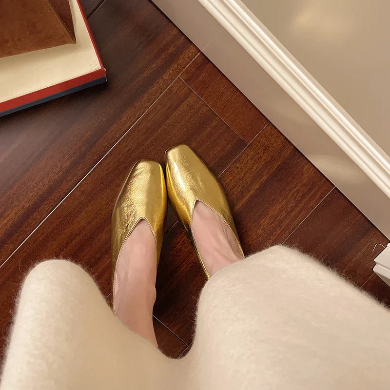 Gold metallic Lyra mules, pointed toe and low block heel, pair on wooden floor