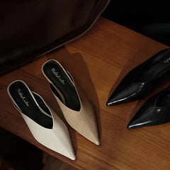 Beige and black leather pointed-toe mules with low heels, slip-on style.