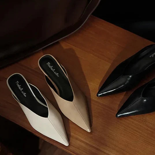 Beige and black leather pointed-toe mules with low heels, slip-on style.