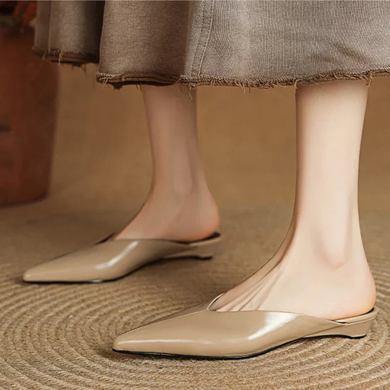 Beige leather mules on feet with pointed toe and low heel