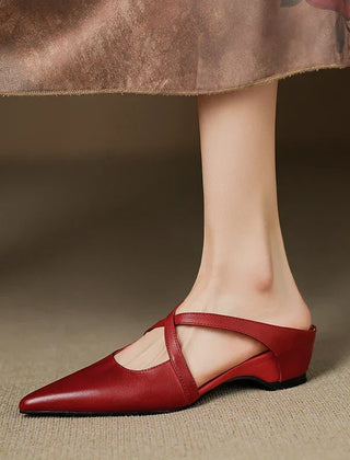 Red leather mules on feet, pointed toe with slingback strap and low block heel.