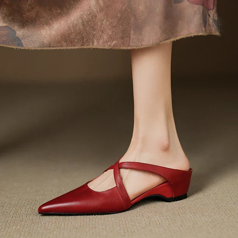Red leather mules on feet, pointed toe with slingback strap and low block heel.