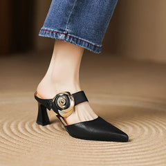 Black leather heels with pointed toe, ankle strap, rosette buckle, and mid block heel