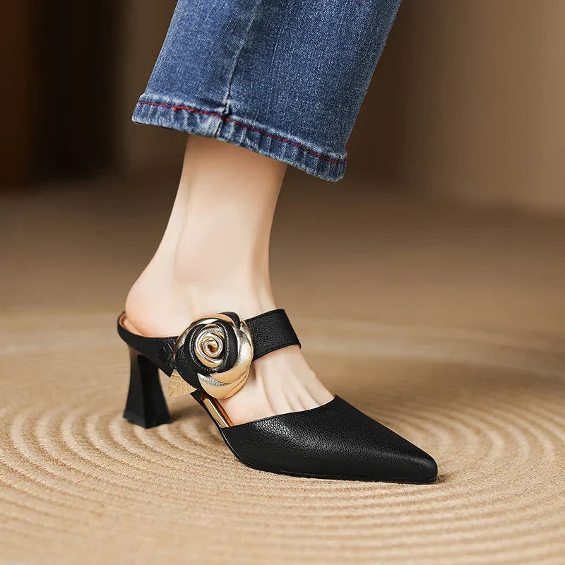 Black leather heels with pointed toe, ankle strap, rosette buckle, and mid block heel