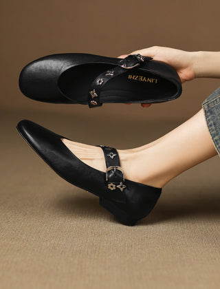 Black leather flats with buckle strap and star-flower studs, low rounded toe