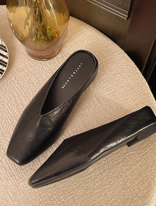 Black pointed-toe mules with low flat heel and slip-on backless design.