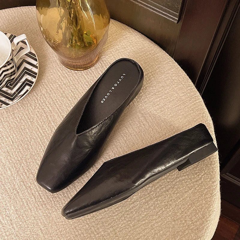 Black pointed-toe mules with low flat heel and slip-on backless design.