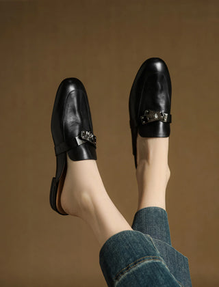 Black leather mules with square-toe and metallic buckle strap worn with jeans