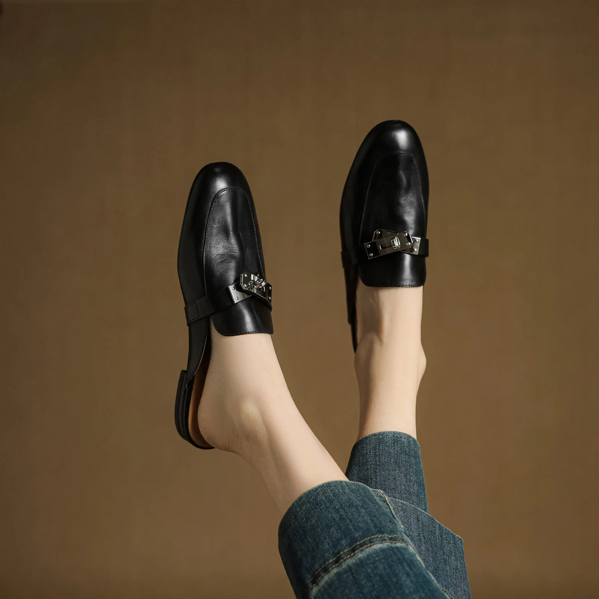 Black leather mules with square-toe and metallic buckle strap worn with jeans