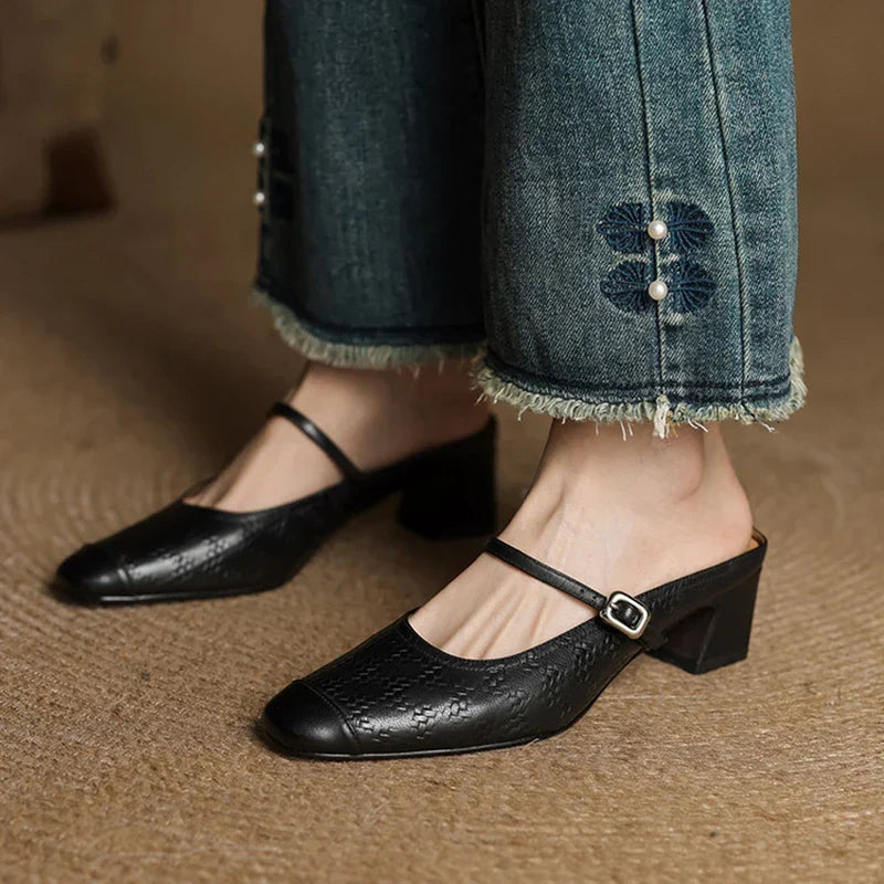 Black leather mule with square toe, buckle strap, and block heel, worn with denim