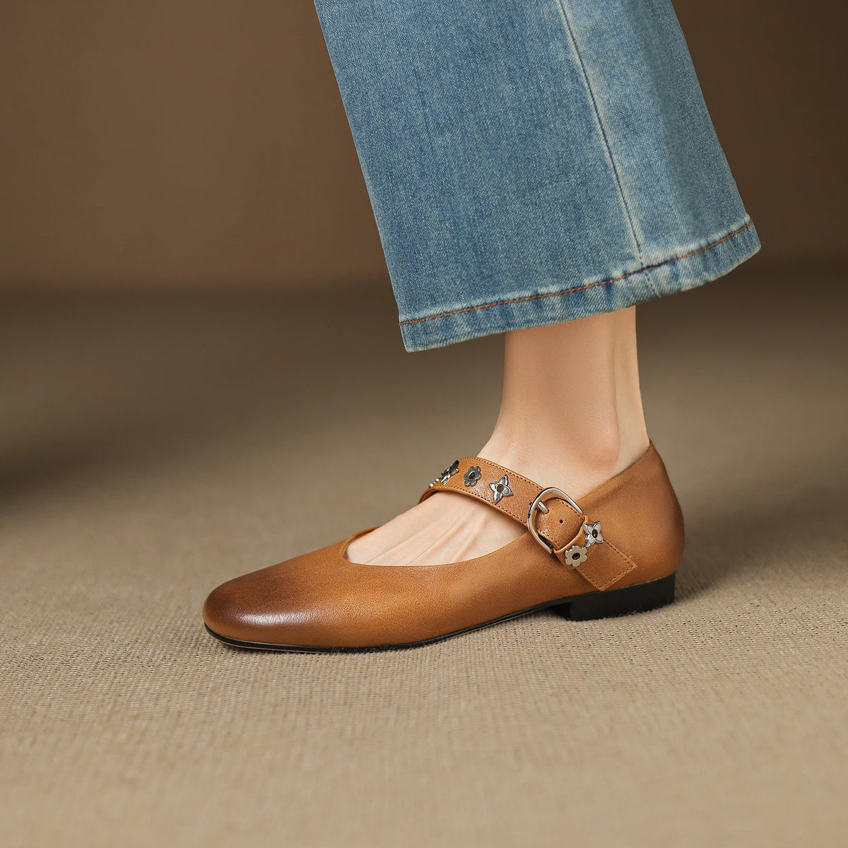 Tan leather flats with decorative buckle strap and star-flower charm accents