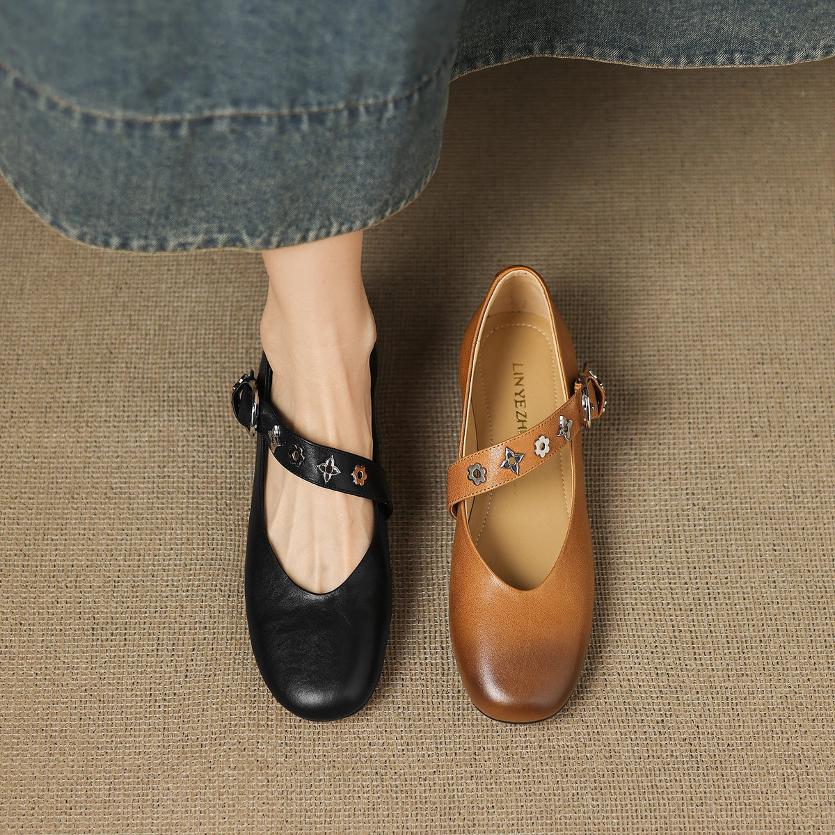 Black leather flats with ankle strap, buckle, and star-flower charm accents