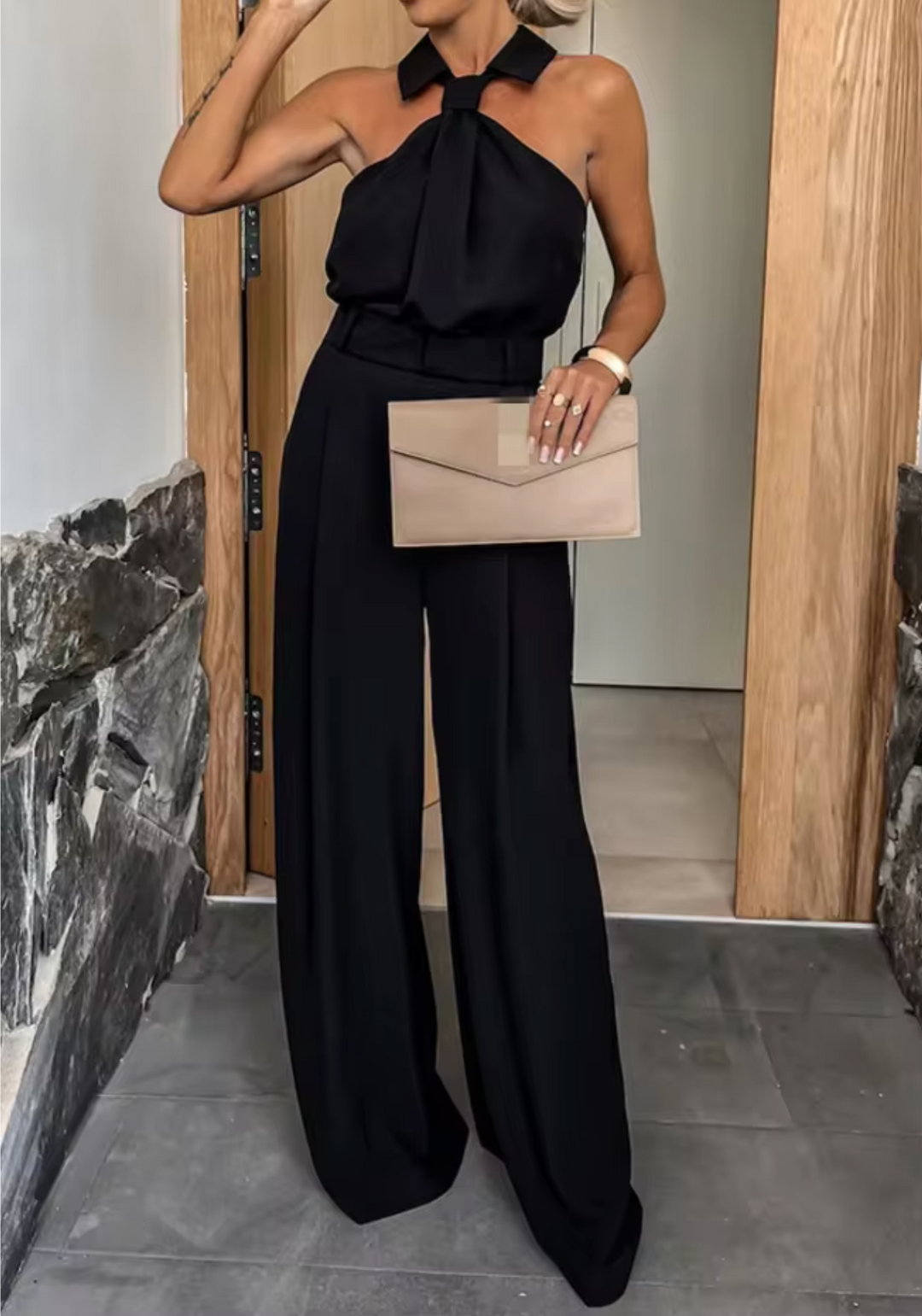 Black halter jumpsuit with neck bow detail and wide-leg trousers, belted waist.