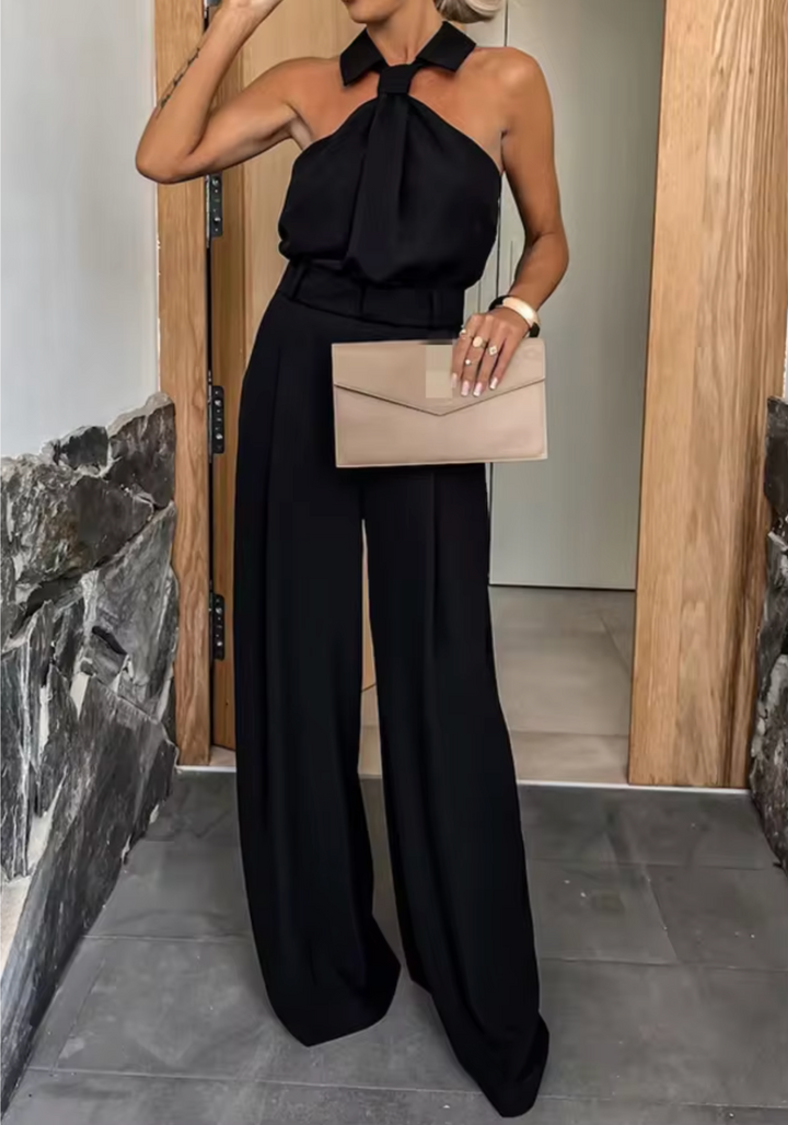 Black halter jumpsuit with neck bow detail and wide-leg trousers, belted waist.