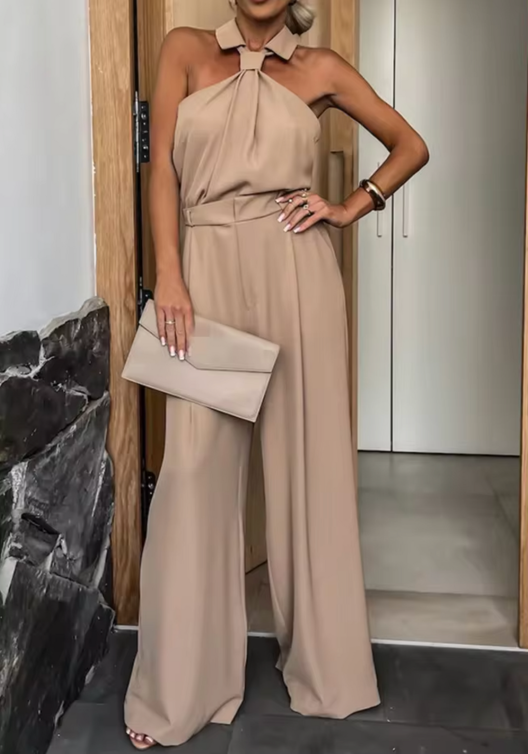 Taupe halter jumpsuit with bow neck and wide-leg pants, belted waist with drape.