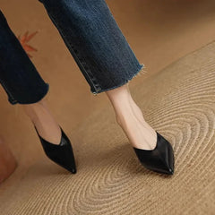 Black leather pointed-toe mules with low heel, side view on feet.