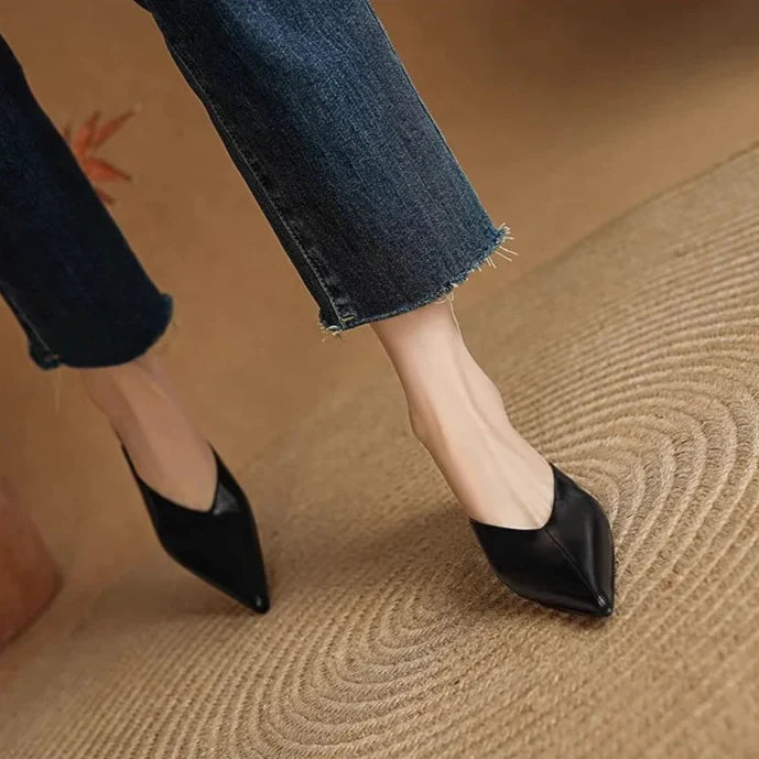 Black leather pointed-toe mules with low heel, side view on feet.