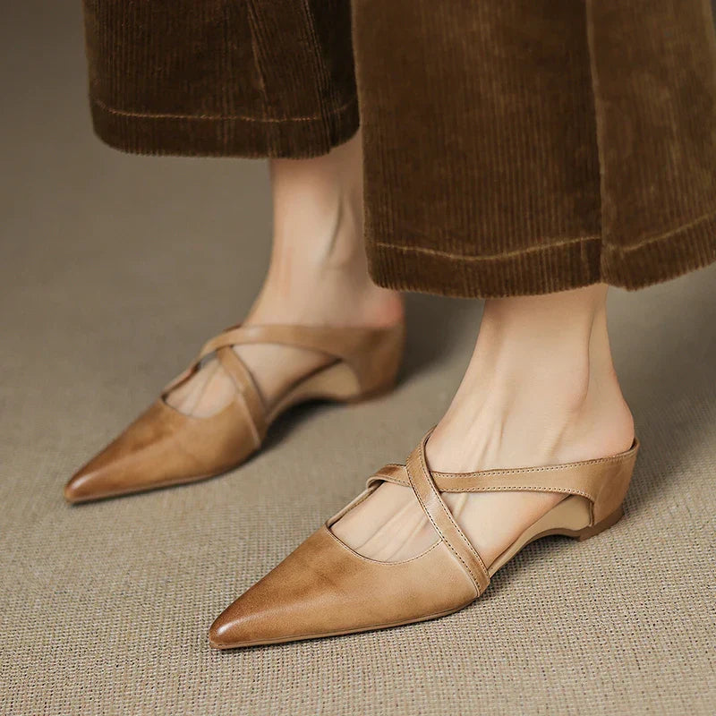Tan leather mules on feet, pointed toe with cross slingback strap and low heel.