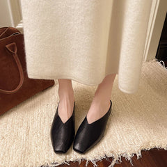 Black pointed-toe slip-on mules with low flat heel and backless design.