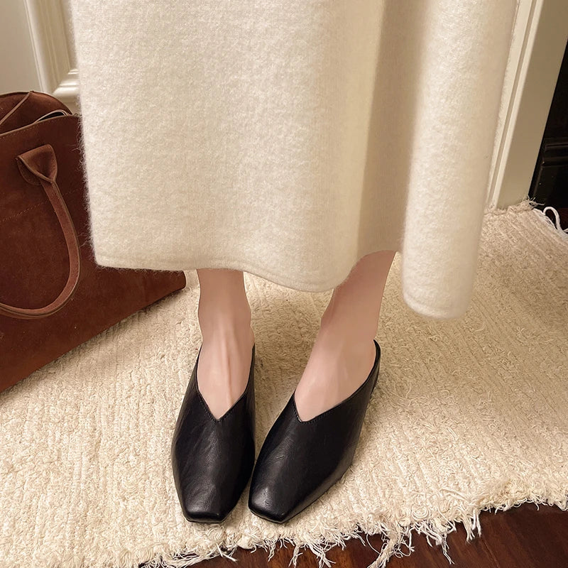 Black pointed-toe slip-on mules with low flat heel and backless design.