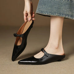 Black leather mules with pointed toe and bow-style buckle strap on feet