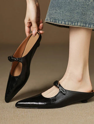 Black leather mules with pointed toe and bow-style buckle strap on feet