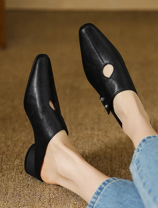 Black leather mules on feet with side cutouts and stud accents, low block heels