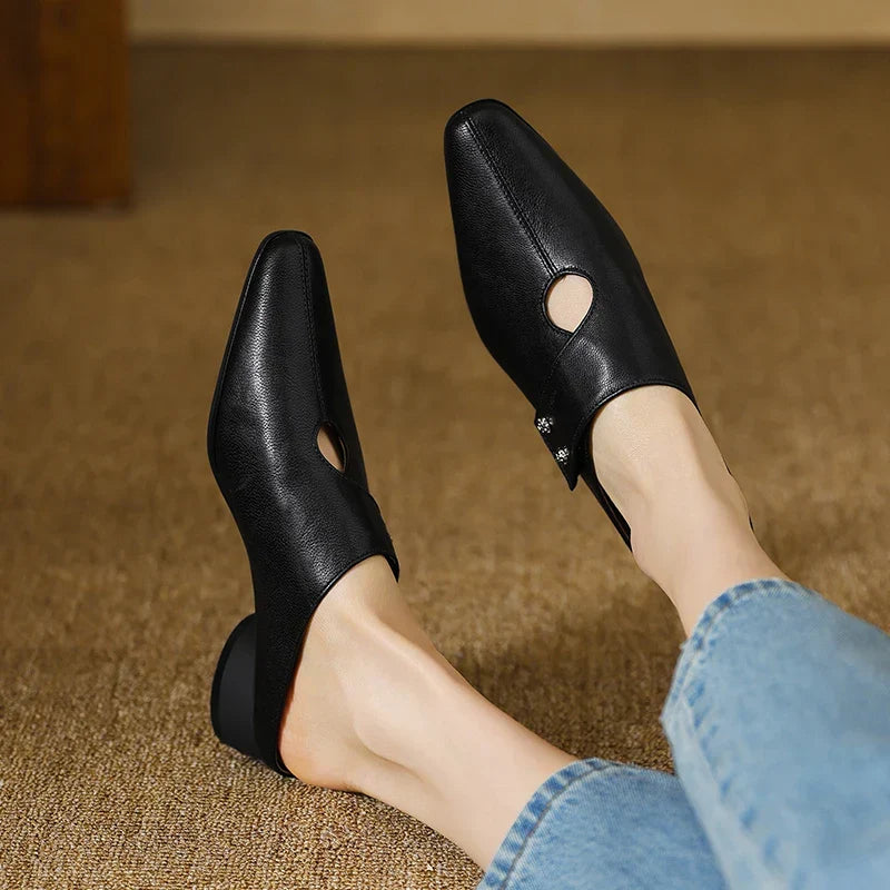 Black leather mules on feet with side cutouts and stud accents, low block heels