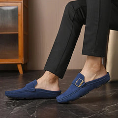 Blue suede mules on model with square metal buckle strap and slip-on design