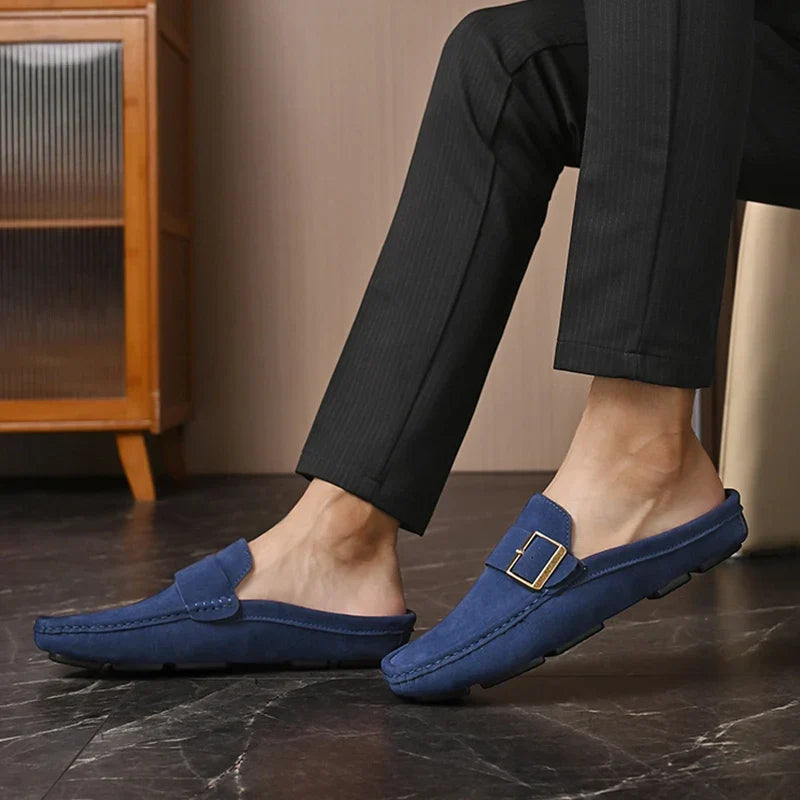 Blue suede mules on model with square metal buckle strap and slip-on design