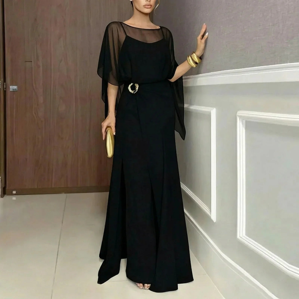 Black long jumpsuit with sheer overlay cape sleeves and ring-buckle waist detail.