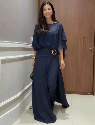 Navy long jumpsuit with sheer overlay cape sleeves and ring-buckle waist detail.