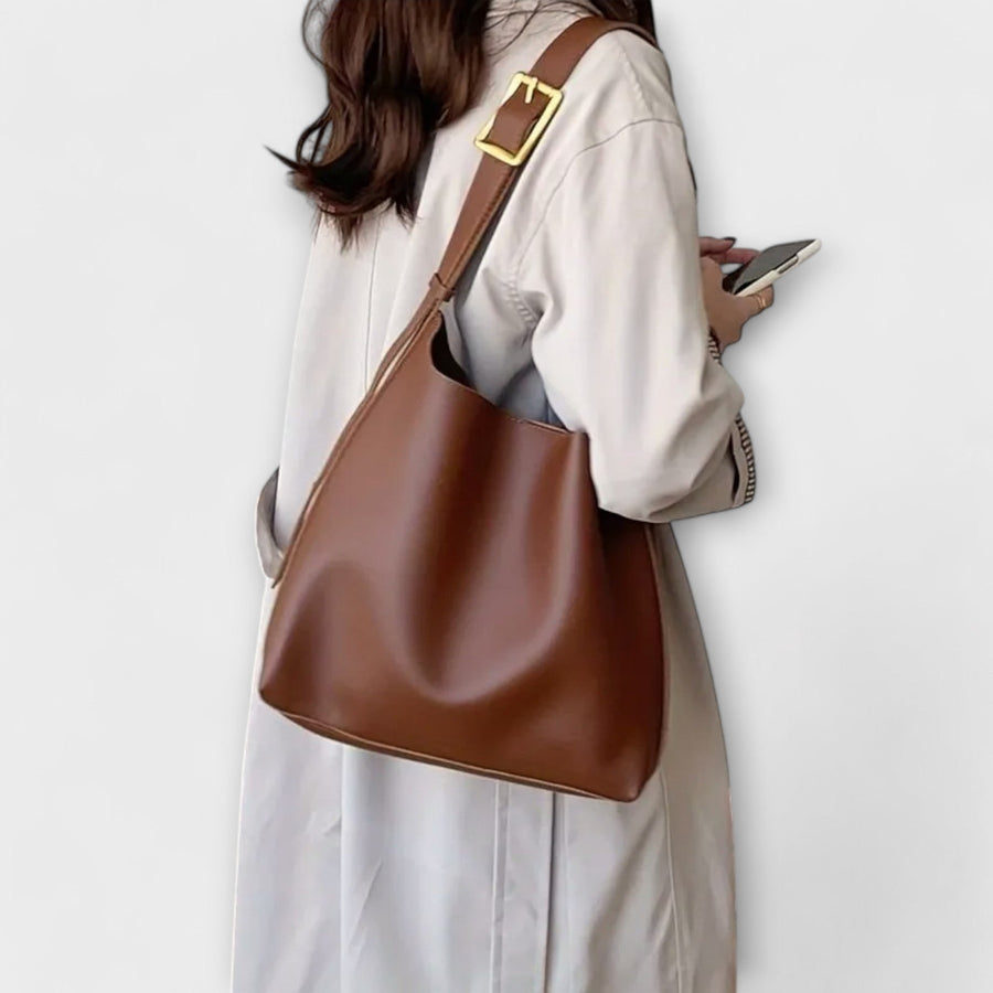 Brown leather shoulder bag carried over shoulder, gold-tone buckle detail