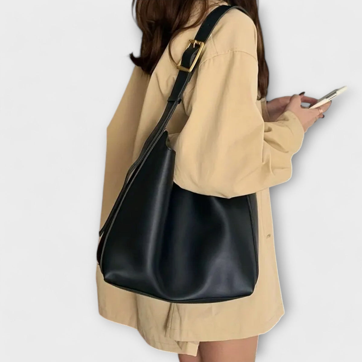 Black leather shoulder bag with top strap and gold-tone buckle, held on model