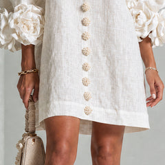 White button-down mini dress hem with vertical gold buttons and rosette puff sleeves